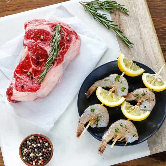 Steak with herbs, plate of lemon and shrimp skewers, bowl of peppercorn
