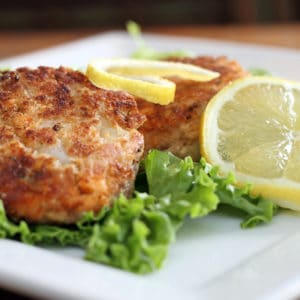 Salmon cakes over green lettuce with lemon slices on a white plate
